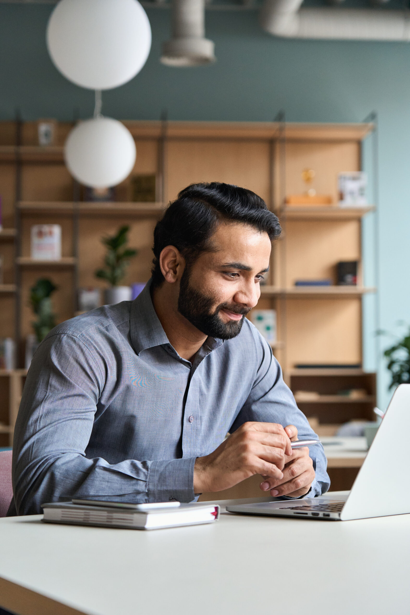 Smiling bearded indian businessman working on laptop at home office. Young indian student using computer remote studying, virtual training on video call meeting, watching online webinar or seminar.