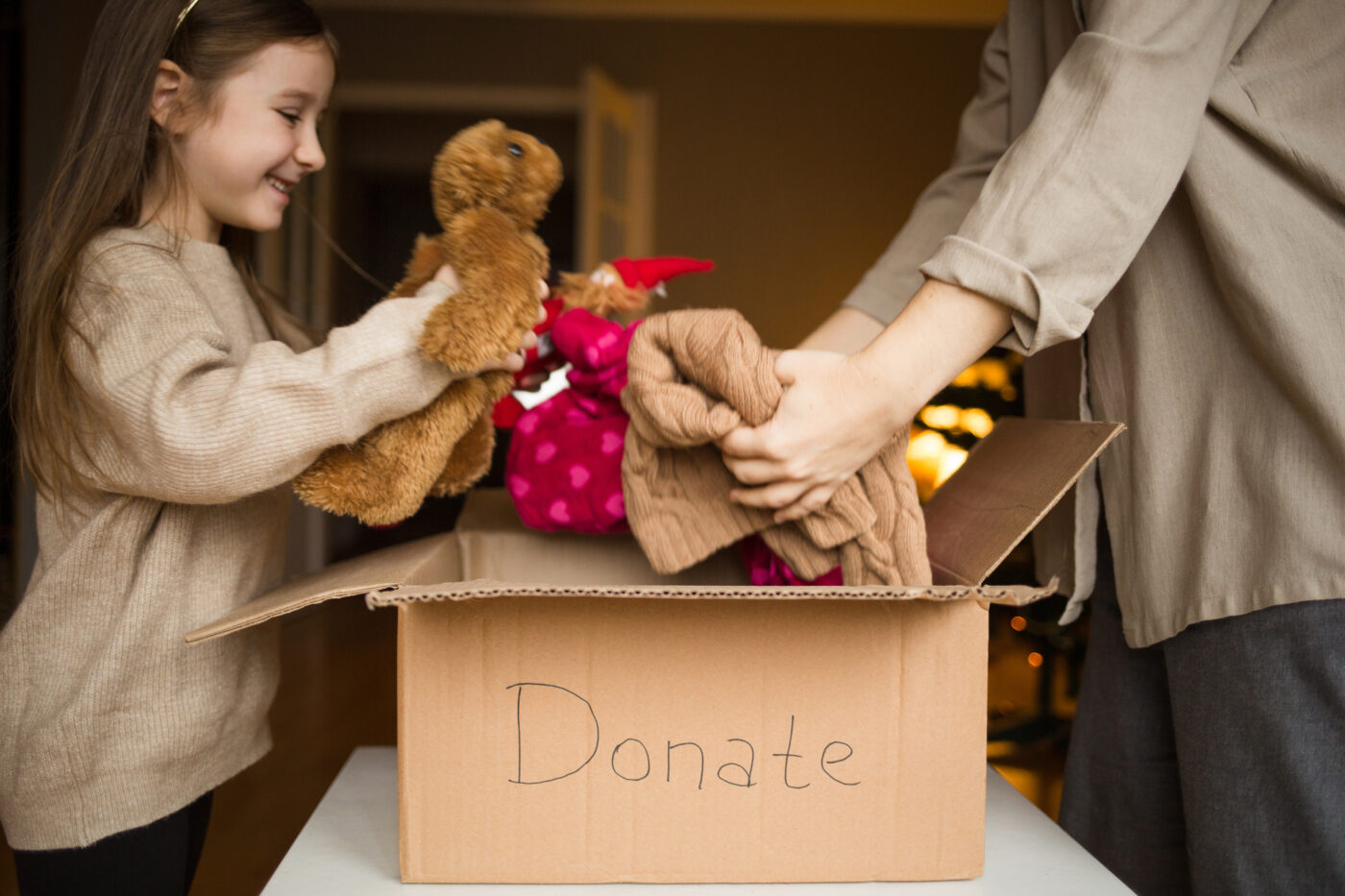 cardboard box with inscription donate. family mother and child put clothes and toys in box at home against background of Christmas tree. donation.